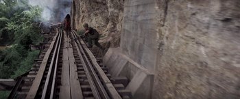 Movie still from “Casualties of War” (1989), directed by Brian De Palma – A man in a green uniform is standing on a train track; Wide shot, High angle