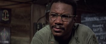 Movie still from “Casualties of War” (1989), directed by Brian De Palma – A person wearing glasses and a green shirt; Close Up shot, Low angle