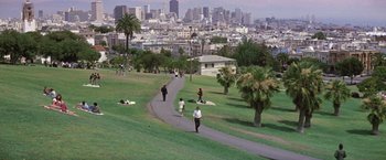 People are walking on a path in a park with a city in the background