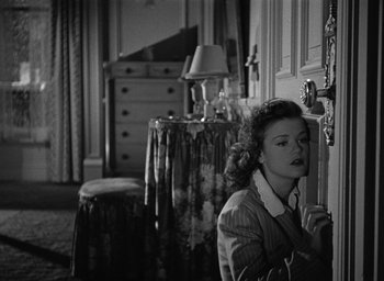 Movie still from “Cat People” (1942), directed by Jacques Tourneur – A black and white photo of a woman looking out of a door; Medium shot, High angle