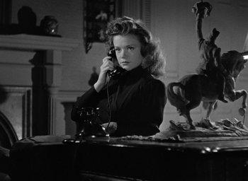 Movie still from “Cat People” (1942), directed by Jacques Tourneur – A woman sitting at a desk talking on a phone; Medium shot, Low angle