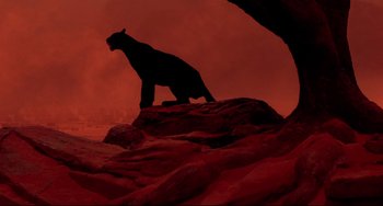 Movie still from “Cat People” (1982), directed by Paul Schrader – A black bear standing on top of a red rock; Wide shot, Low angle