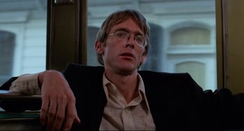 Movie still from “Cat People” (1982), directed by Paul Schrader – A man with glasses sitting in a chair looking at the camera; Close Up shot, Low angle