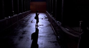 Movie still from “Cat People” (1982), directed by Paul Schrader – A person standing in a dark alley holding a cell phone; Extreme Wide shot, High angle