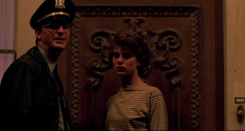Movie still from “Cat People” (1982), directed by Paul Schrader – A man standing next to a woman in front of an ornate wall; Medium shot, Low angle