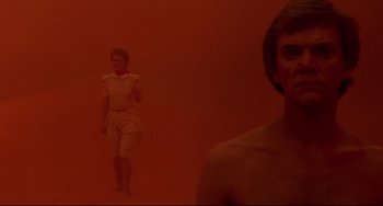 Movie still from “Cat People” (1982), directed by Paul Schrader – A man standing next to another man in a red room; Medium shot, Low angle