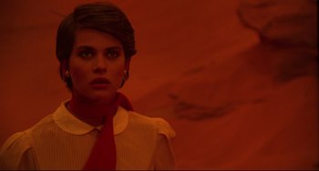 Movie still from “Cat People” (1982), directed by Paul Schrader – A woman with a red neck tie standing in front of an orange background; Close Up shot, Over the shoulder angle