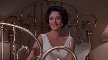 Movie still from “Cat on a Hot Tin Roof” (1958), directed by Richard Brooks – A woman sitting on a bed wearing a white dress; Medium shot, Low angle