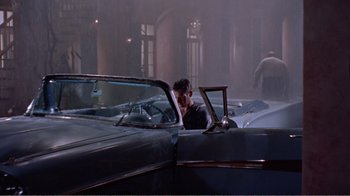 Movie still from “Cat on a Hot Tin Roof” (1958), directed by Richard Brooks – A man sitting in the back seat of a vintage car; Wide shot, Over the shoulder angle