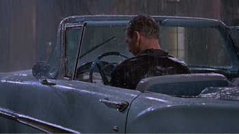 Movie still from “Cat on a Hot Tin Roof” (1958), directed by Richard Brooks – A man sitting in the driver's seat of an old car; Wide shot, High angle