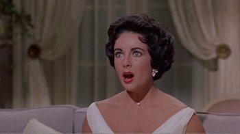 Movie still from “Cat on a Hot Tin Roof” (1958), directed by Richard Brooks – A person sitting on a couch wearing a dress; Close Up shot, High angle