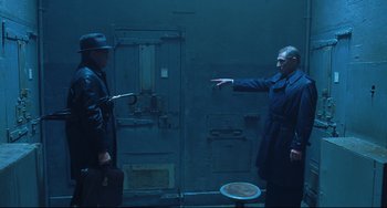 Movie still from “Catch Me If You Can” (2002), directed by Steven Spielberg – A man in a trench coat pointing at another man; Wide shot, High angle