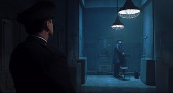 Movie still from “Catch Me If You Can” (2002), directed by Steven Spielberg – A man standing in front of another man in a dark room; Wide shot, High angle