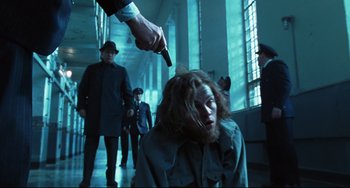 Movie still from “Catch Me If You Can” (2002), directed by Steven Spielberg – A man is pointing a gun at a woman in a hallway; Medium shot, Low angle