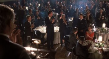 Movie still from “Catch Me If You Can” (2002), directed by Steven Spielberg – A group of men in suits and ties standing in front of a table; Wide shot, Over the shoulder angle