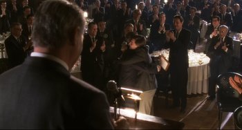 Movie still from “Catch Me If You Can” (2002), directed by Steven Spielberg – A man hugging another man in front of an audience; Medium shot, Over the shoulder angle