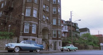Movie still from “Catch Me If You Can” (2002), directed by Steven Spielberg – An old car parked in front of an apartment building; Extreme Wide shot, Low angle