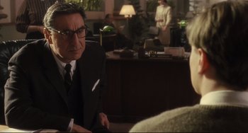 Movie still from “Catch Me If You Can” (2002), directed by Steven Spielberg – A man wearing a suit and tie sitting at a table; Medium shot, Over the shoulder angle