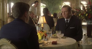 Movie still from “Catch Me If You Can” (2002), directed by Steven Spielberg – A man sitting at a table in front of another man in a suit; Medium shot, Over the shoulder angle