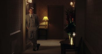 Movie still from “Catch Me If You Can” (2002), directed by Steven Spielberg – A man in a suit and tie standing in front of a vase of flowers; Wide shot, Low angle