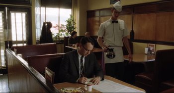 Movie still from “Catch Me If You Can” (2002), directed by Steven Spielberg – A man sitting at a table in front of a plate of food; Medium shot, Over the shoulder angle
