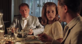 Movie still from “Catch Me If You Can” (2002), directed by Steven Spielberg – A young girl sitting at a dinner table with her family; Medium shot, Over the shoulder angle