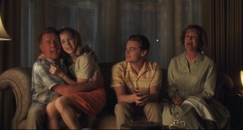 Movie still from “Catch Me If You Can” (2002), directed by Steven Spielberg – A group of people sitting on top of a brown couch; Medium shot, Over the shoulder angle
