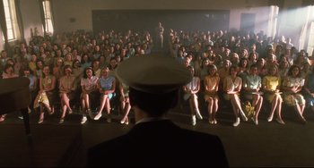 Movie still from “Catch Me If You Can” (2002), directed by Steven Spielberg – A group of people sitting in front of a man in a hat; Wide shot, High angle