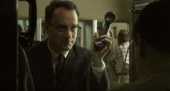 Movie still from “Catch Me If You Can” (2002), directed by Steven Spielberg – A man in a suit and tie holding a hair dryer; Close Up shot, Over the shoulder angle