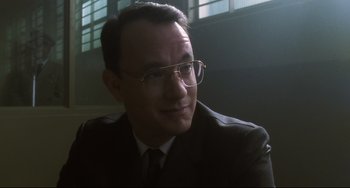 Movie still from “Catch Me If You Can” (2002), directed by Steven Spielberg – A man in a suit and tie wearing glasses; Close Up shot, Over the shoulder angle