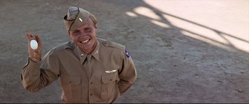 Movie still from “Catch-22” (1970), directed by Mike Nichols – A man in a military uniform smiling for the camera; Medium shot, Low angle