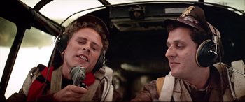 Movie still from “Catch-22” (1970), directed by Mike Nichols – Two young men are in a helicopter and one of them is holding a camera; Medium shot, Low angle