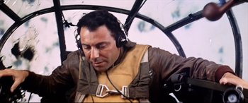 Movie still from “Catch-22” (1970), directed by Mike Nichols – A man with headphones is sitting in an airplane; Medium shot, Low angle
