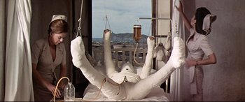 Movie still from “Catch-22” (1970), directed by Mike Nichols – A person in a hospital bed holding a glass of beer; Wide shot, Low angle