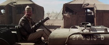 Movie still from “Catch-22” (1970), directed by Mike Nichols – A man sitting on top of a motorcycle in the dirt; Wide shot, Over the shoulder angle