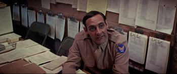 Movie still from “Catch-22” (1970), directed by Mike Nichols – A man sitting at a table with papers on the wall behind him; Close Up shot, Low angle