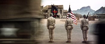 Movie still from “Catch-22” (1970), directed by Mike Nichols – Two men standing in front of an american flag and an old house; Wide shot, Low angle
