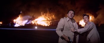 Movie still from “Catch-22” (1970), directed by Mike Nichols – A man standing in front of a burning building at night; Medium shot, Low angle