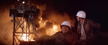 Movie still from “Catch-22” (1970), directed by Mike Nichols – A man wearing a helmet laughing in front of a fire; Medium shot, Low angle