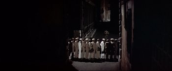 Movie still from “Catch-22” (1970), directed by Mike Nichols – A group of men standing next to each other in front of a building; Extreme Wide shot, High angle