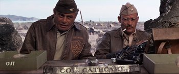 Movie still from “Catch-22” (1970), directed by Mike Nichols – A couple of men sitting next to each other at a table; Medium shot, Over the shoulder angle
