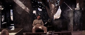 Movie still from “Catch-22” (1970), directed by Mike Nichols – A man sitting on a chair in front of a wall; Wide shot, Low angle