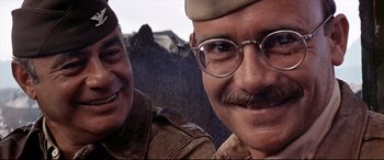 Movie still from “Catch-22” (1970), directed by Mike Nichols – A man with glasses and a mustache and a man with a mustache and a hat; Close Up shot, Low angle