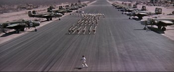 Movie still from “Catch-22” (1970), directed by Mike Nichols – A man walking across an airport runway towards a herd of zebra; Extreme Wide shot, High angle
