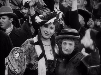 Movie still from “Cavalcade” (1933), directed by Frank Lloyd – Two women are standing in a crowd wearing hats; Medium shot, High angle