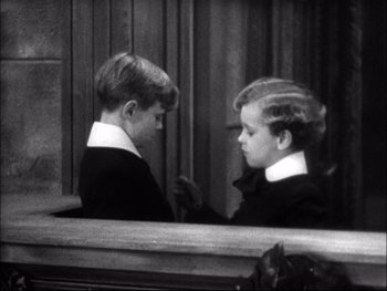 Movie still from “Cavalcade” (1933), directed by Frank Lloyd – Two young boys talking in front of a wooden wall; Medium shot, High angle
