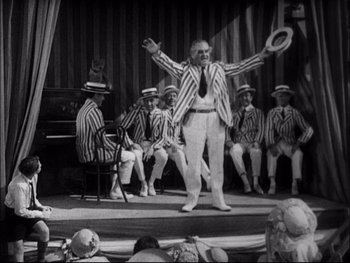 Movie still from “Cavalcade” (1933), directed by Frank Lloyd – An old photo of a man on a stage with a bunch of people; Wide shot, Low angle