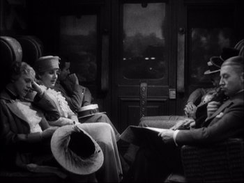 Movie still from “Cavalcade” (1933), directed by Frank Lloyd – Two people sitting on a train with hats on; Medium shot, High angle