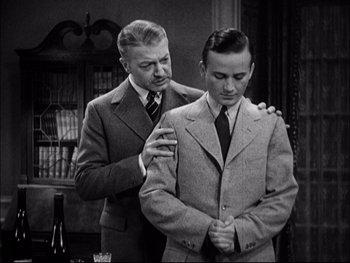 Movie still from “Cavalcade” (1933), directed by Frank Lloyd – A man in a suit and tie is standing next to another man in a suit and tie; Medium shot, Over the shoulder angle