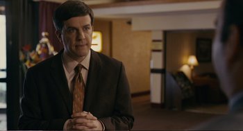 Movie still from “Cedar Rapids” (2011), directed by Miguel Arteta – A man wearing a suit and tie in a room; Medium shot, Over the shoulder angle
